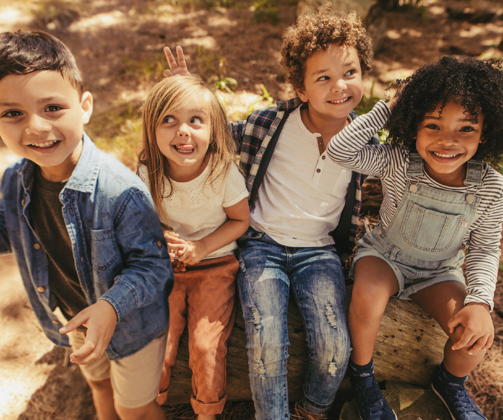 4 smiling kids sitting on a piece of wood in the forest Speedy Monkey 